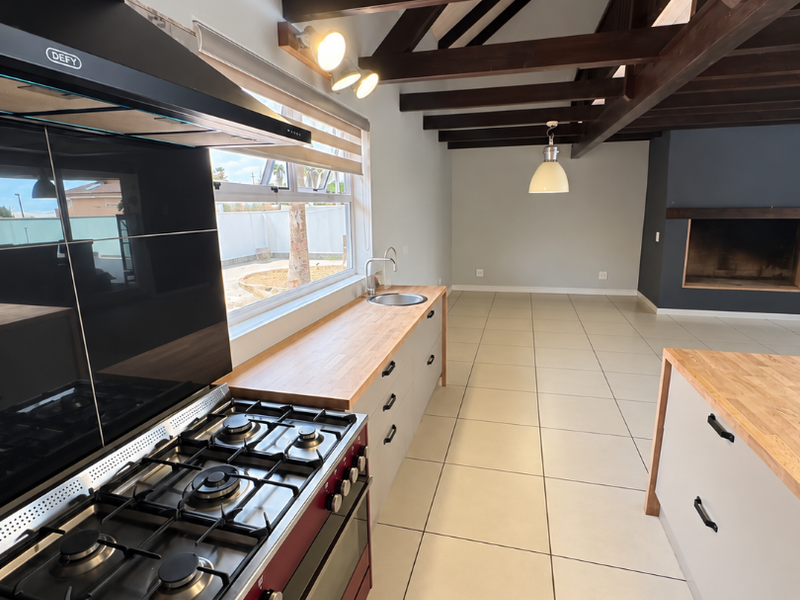 Spacious open-plan kitchen and living area featuring vaulted ceilings with exposed timber beams, modern cabinetry, wooden countertops, and a built-in fireplace.