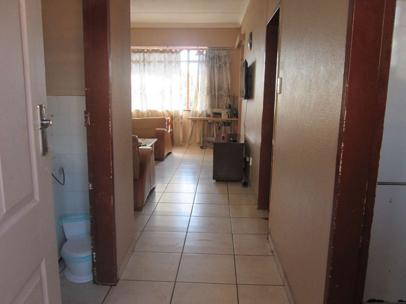 A view through a hallway with tiled flooring leading into a living area, showing dated finishes and worn door frames.