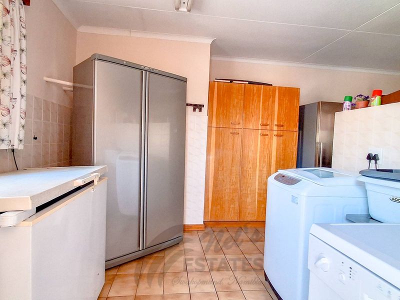 A functional laundry room featuring tiled flooring, built-in wooden cabinetry, and tiled splashbacks, providing ample space for utility appliances and storage.