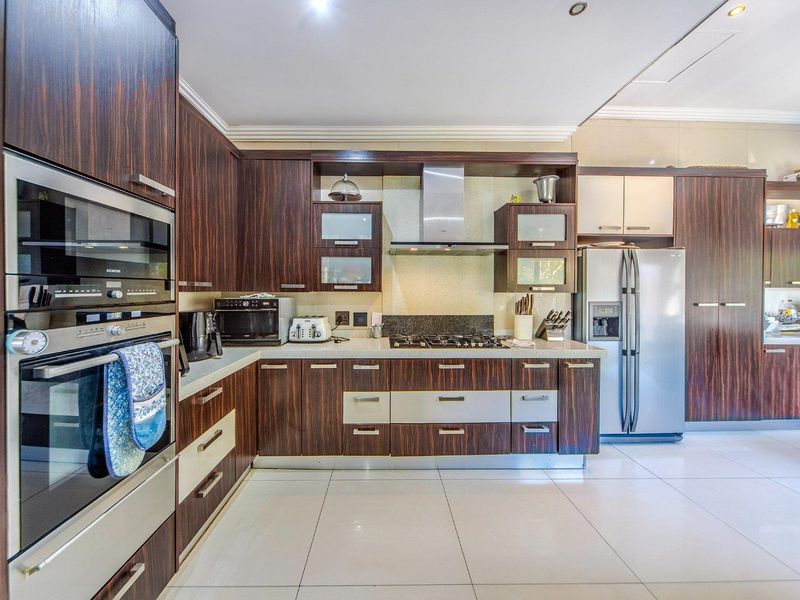 Modern kitchen featuring dark wood cabinetry, stone countertops, integrated stainless steel appliances, gas hob, and large format floor tiles.