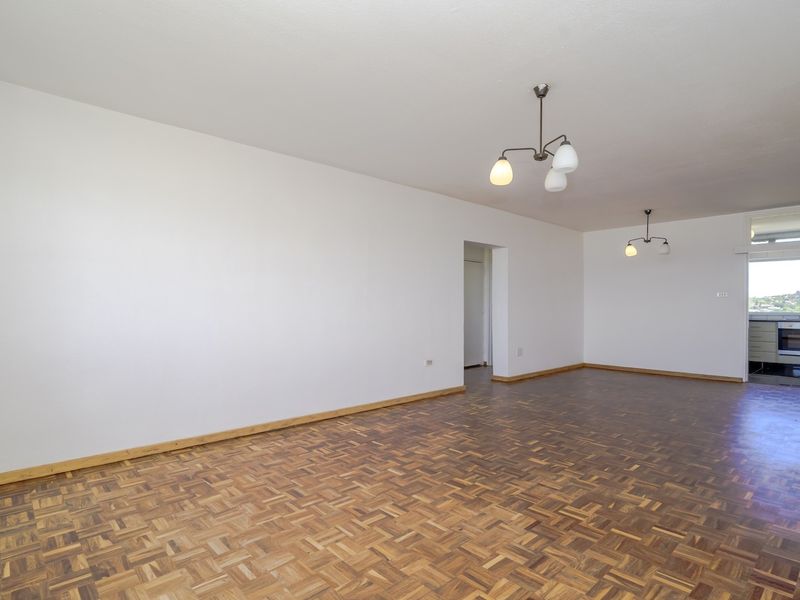 Spacious open-plan living area featuring classic parquet flooring and a view into the adjacent kitchen space.