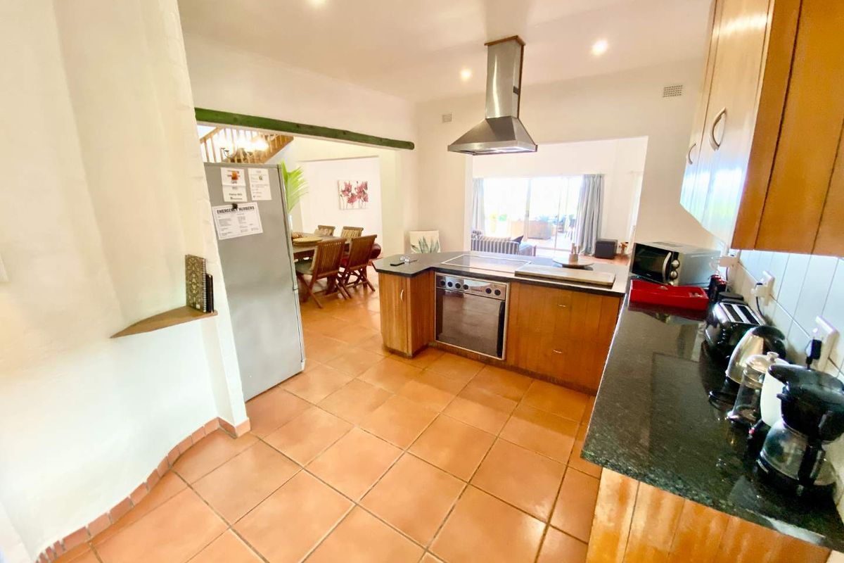 Open-plan kitchen featuring wooden cabinetry, granite countertops, and integrated appliances, flowing into a dining and living area with access to the patio.