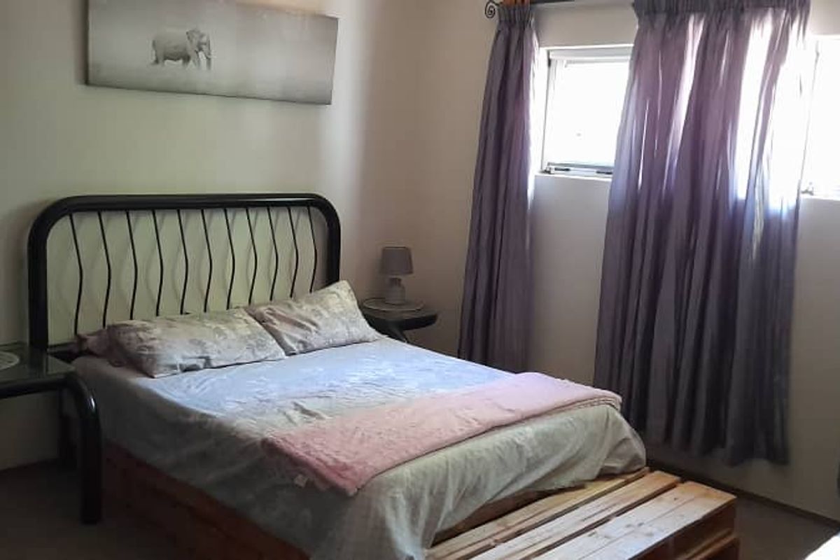 A standard bedroom featuring neutral walls, carpeted flooring, and windows with curtain treatments.