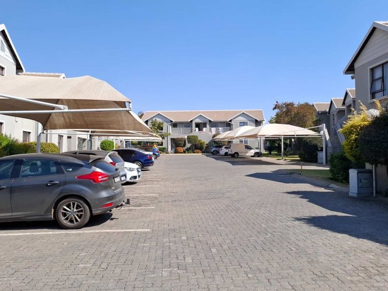 A view of the apartment complex parking area featuring paved driveways and covered shade cloth parking bays for residents.