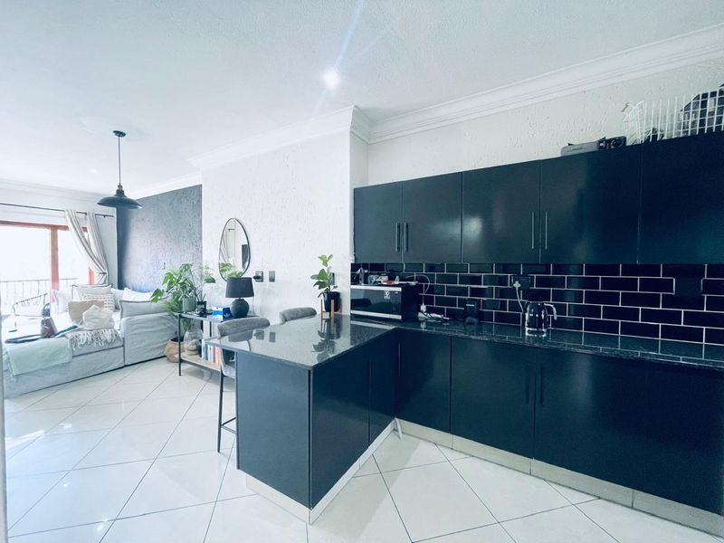 Modern open-plan living area featuring a sleek kitchen with black gloss cabinetry, granite countertops, and a breakfast bar, seamlessly flowing into the lounge space.