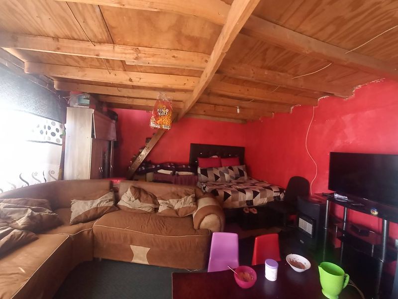 Open-plan living and sleeping area featuring exposed timber ceiling beams and plywood ceiling, requiring significant cosmetic updates and finishing work.