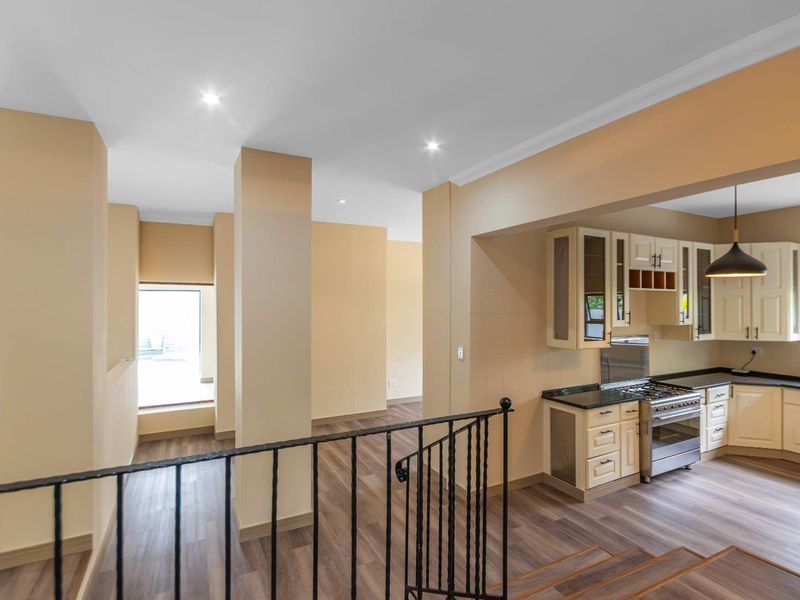 Open plan living area featuring a functional kitchen with built-in cabinetry, gas stove, and modern laminate flooring, overlooking a staircase with wrought iron balustrade.