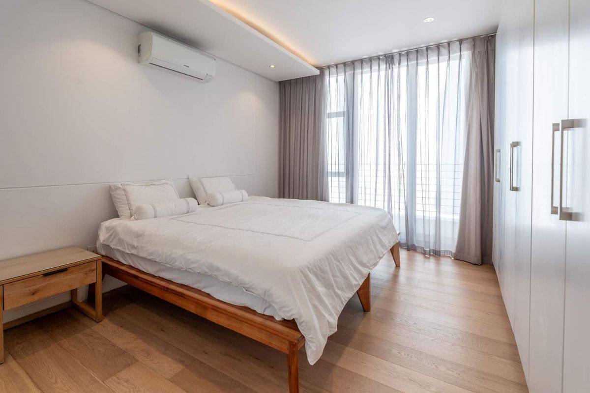 A modern, well-maintained bedroom featuring timber flooring, built-in wardrobes, recessed ceiling lighting, and a wall-mounted split-system air conditioner.