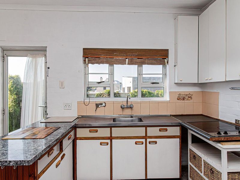 Functional kitchen featuring granite countertops, built-in cabinetry, electric hob, and a stainless steel sink with direct access to the exterior.
