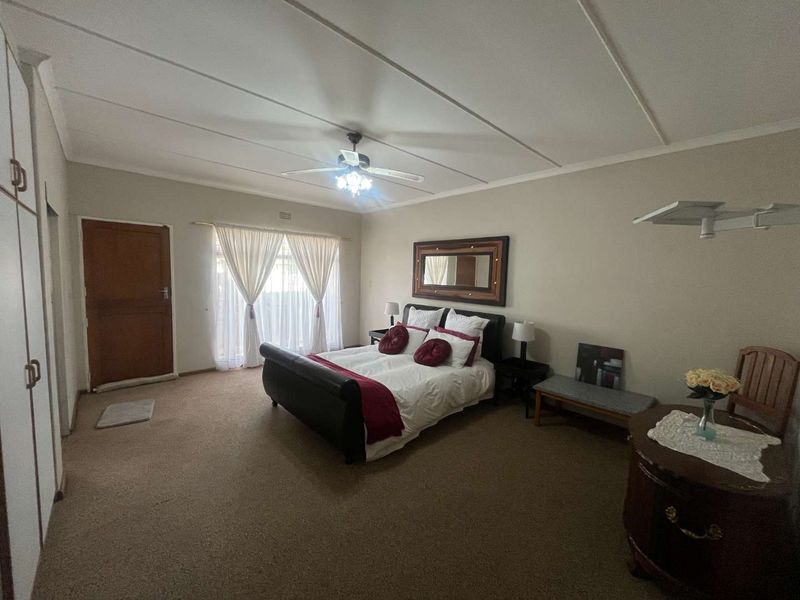 Spacious bedroom featuring neutral walls, carpeted flooring, built-in cupboards, and a ceiling fan, offering a comfortable and functional living space.