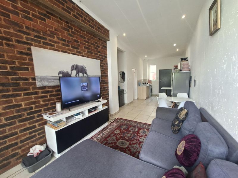 Open-plan living area featuring an exposed brick wall, tiled flooring, and an integrated kitchen space with neutral finishes.