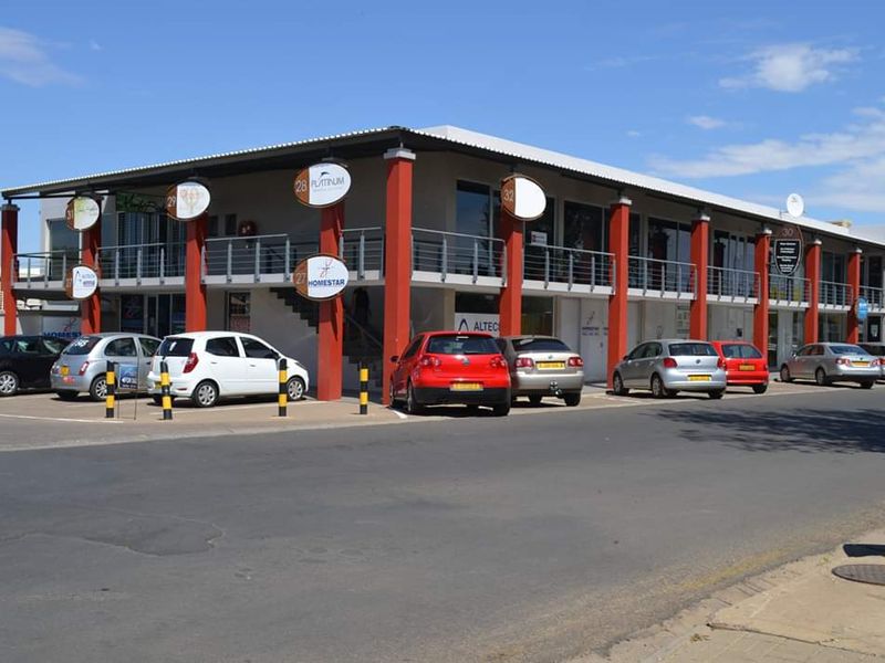 A two-story commercial office building featuring a covered balcony, external staircase, and dedicated paved parking area for tenants and visitors.