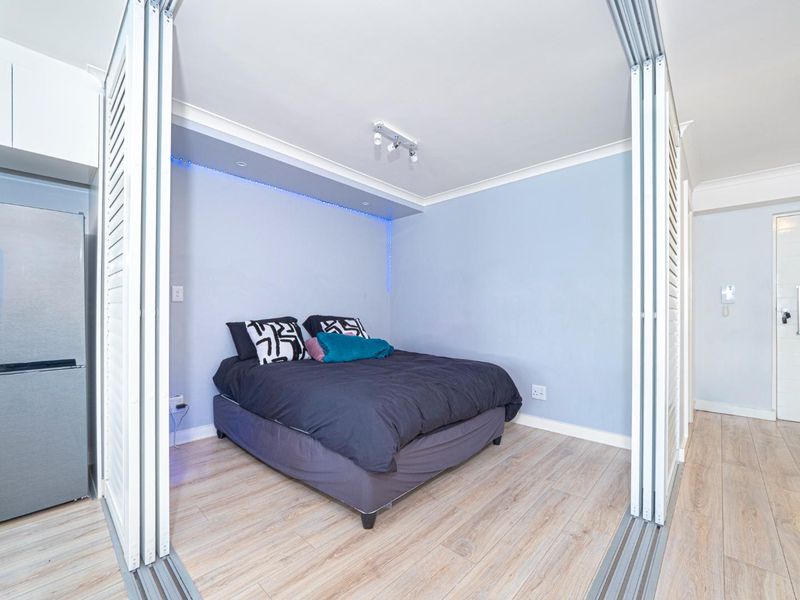 A compact bedroom featuring light wood-look laminate flooring, sliding partition doors for privacy, and modern recessed LED accent lighting.