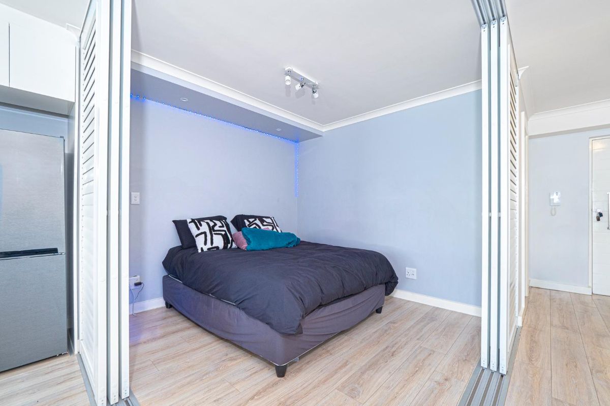 A compact bedroom featuring light wood-look laminate flooring, sliding partition doors for privacy, and modern recessed LED accent lighting.