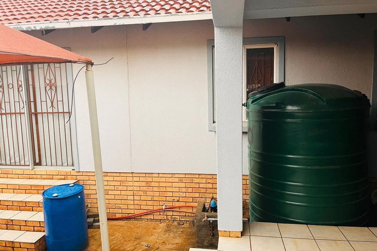 Rear exterior view featuring a covered patio area with tiled flooring, brick base detailing, and a large water storage tank.