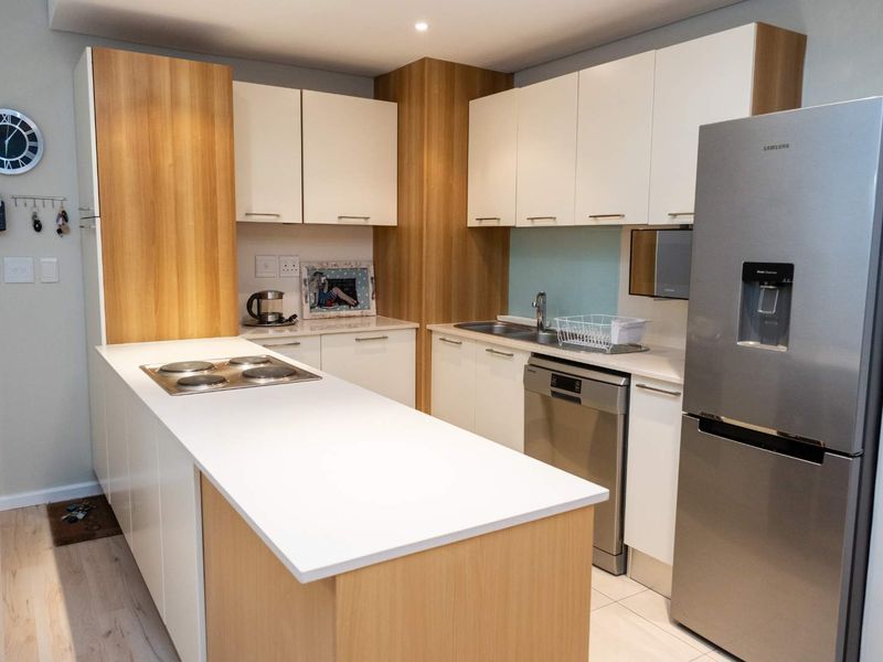 Modern kitchen featuring sleek white and wood-grain cabinetry, stone countertops, a built-in electric hob, and integrated dishwasher.