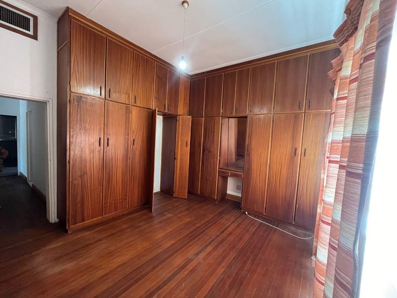 A spacious bedroom featuring extensive floor-to-ceiling built-in wooden cabinetry, a integrated vanity, and original hardwood flooring.