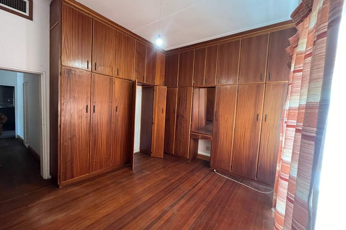 A spacious bedroom featuring extensive floor-to-ceiling built-in wooden cabinetry, a integrated vanity, and original hardwood flooring.