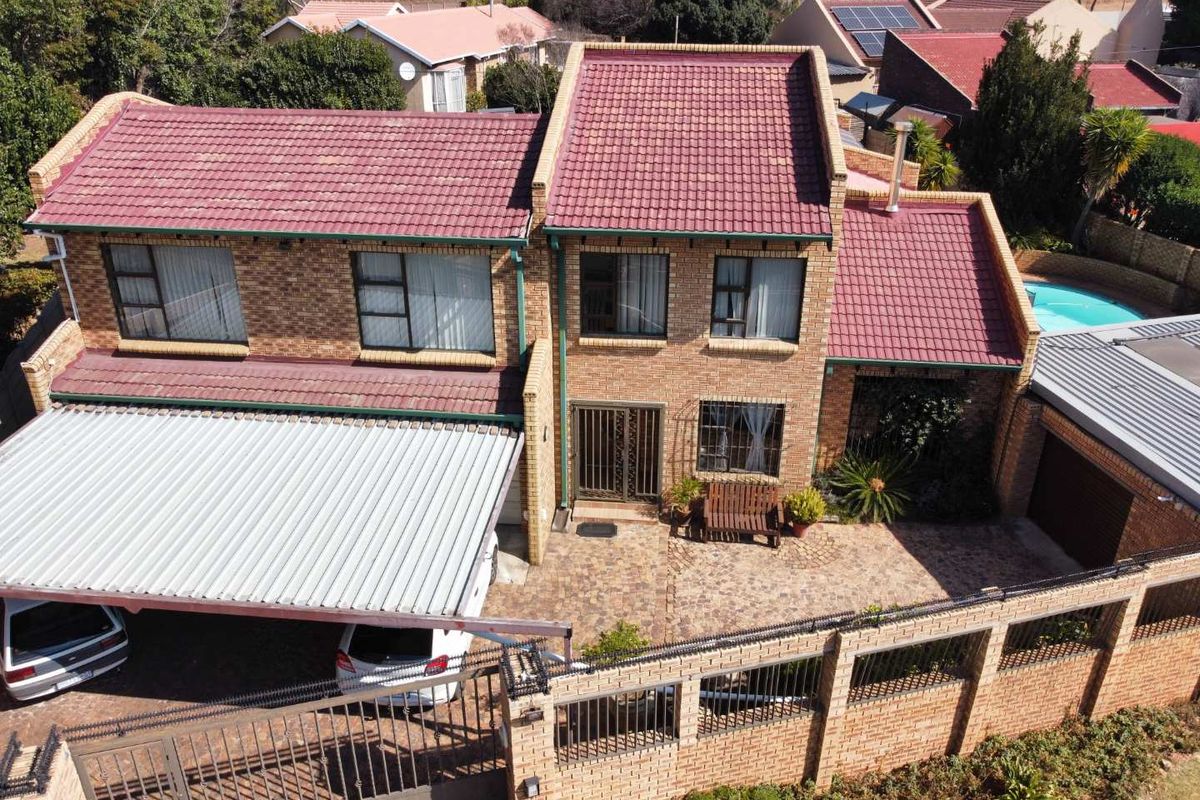 Aerial view of a double-story brick house featuring a tiled roof, paved driveway, carport, and a swimming pool in the rear.