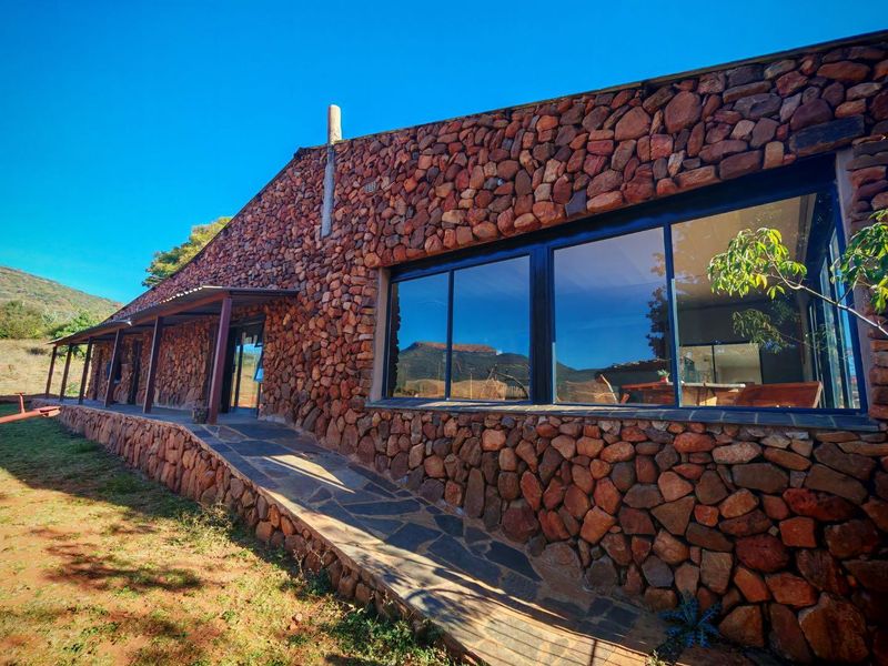 A rear exterior view of a building featuring distinctive natural stone cladding, large sliding glass doors, and a stone-paved ramp leading to a covered walkway.