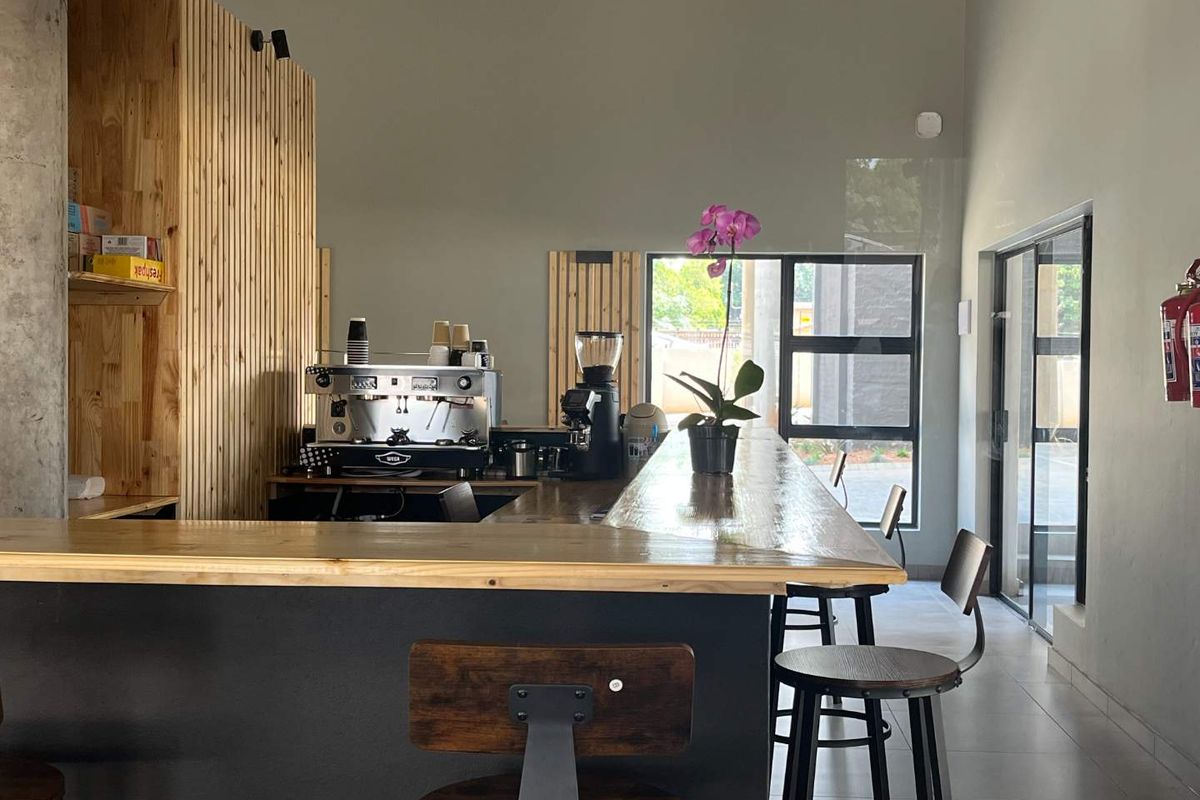 A modern kitchen area featuring a timber-clad feature wall, a spacious timber breakfast bar, and large windows providing natural light.