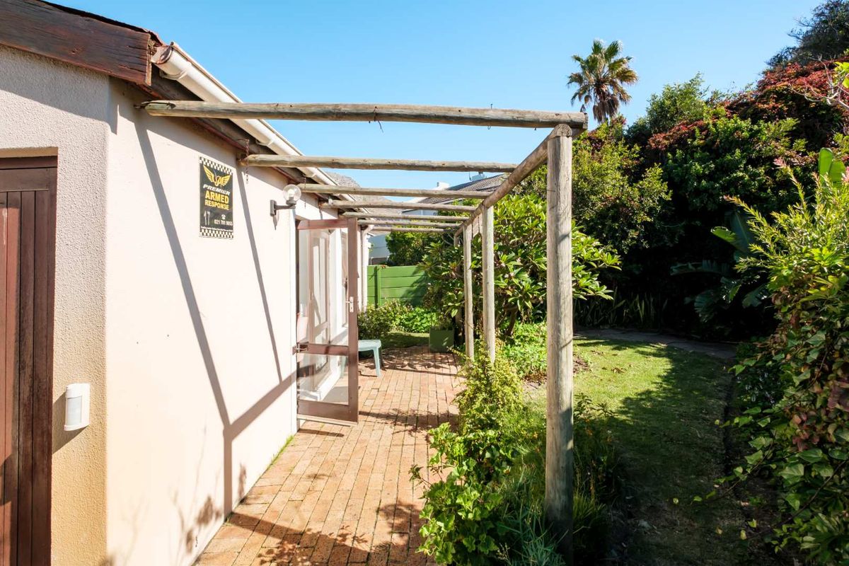 A rear exterior view featuring a brick-paved patio area covered by a timber pergola, adjacent to a landscaped garden.