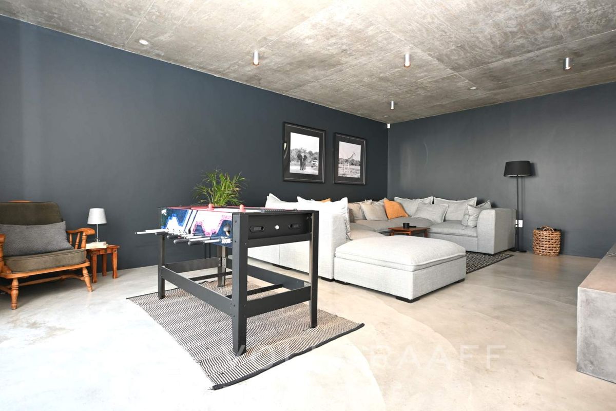 Spacious living area featuring a modern industrial aesthetic with exposed concrete ceilings, polished concrete floors, and dark feature walls.