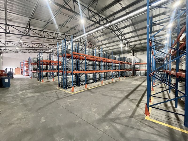 Spacious industrial warehouse featuring high-bay lighting, exposed steel roof trusses, durable concrete flooring, and extensive integrated steel racking systems for storage.