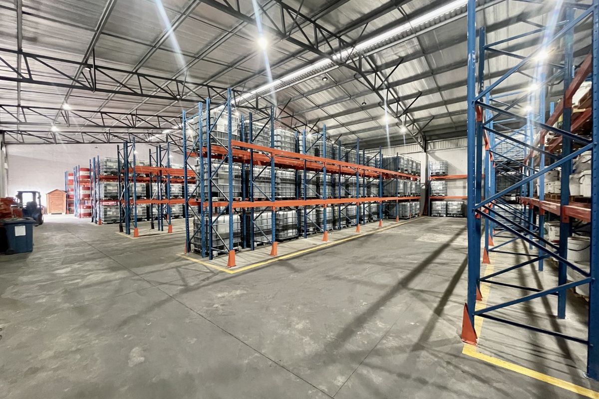 Spacious industrial warehouse featuring high-bay lighting, exposed steel roof trusses, durable concrete flooring, and extensive integrated steel racking systems for storage.