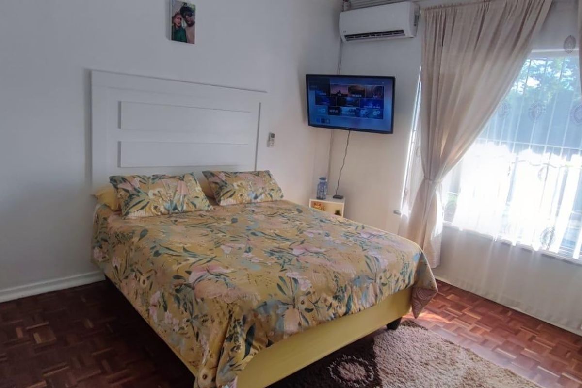 A bedroom featuring parquet flooring, a wall-mounted air conditioning unit, and a built-in headboard, with natural light entering through the window.