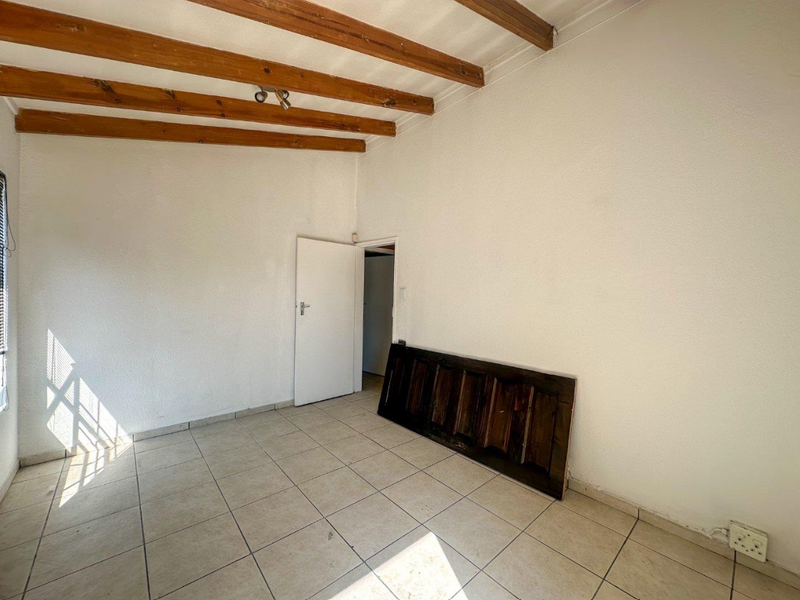 An empty bedroom featuring exposed timber ceiling beams, tiled flooring, and a neutral wall finish, offering a blank canvas for renovation.