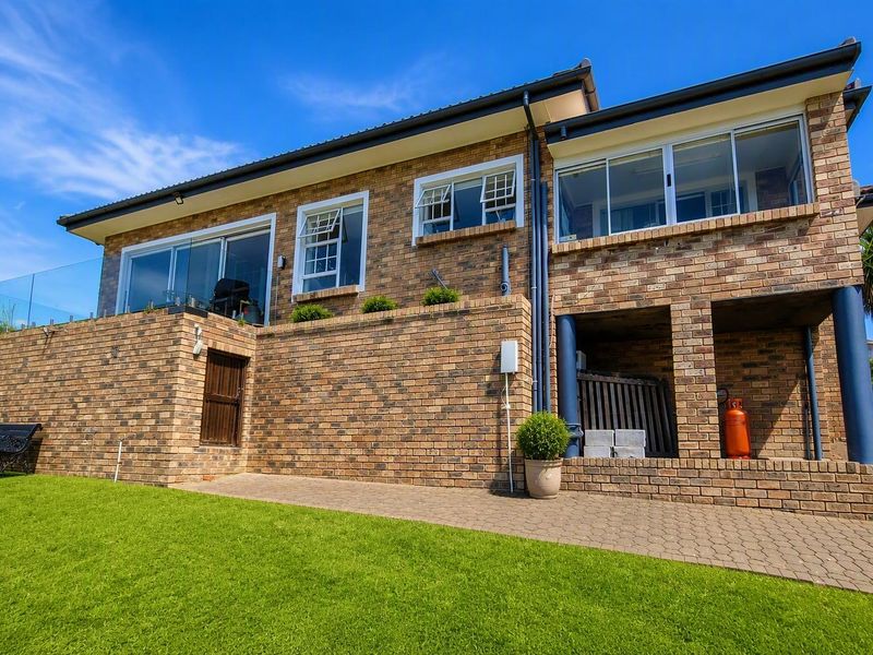 Rear view of a two-story brick house featuring a paved patio area, glass balustrade, and upper-level windows overlooking the garden.