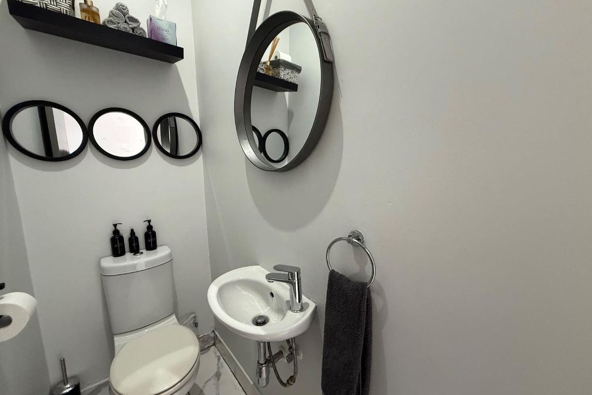 A compact powder room featuring a modern wall-mounted basin with chrome fixtures and a standard toilet, finished with clean white walls and tiled flooring.