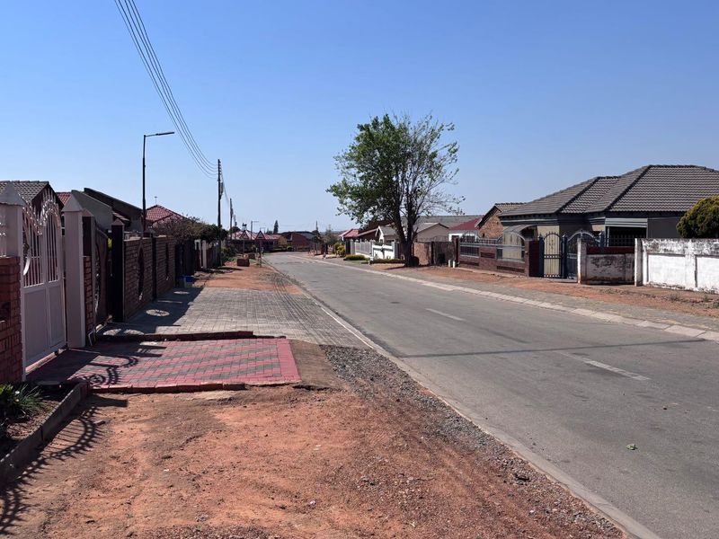 A view of the residential street showing paved sidewalks, boundary walls, and surrounding suburban housing.
