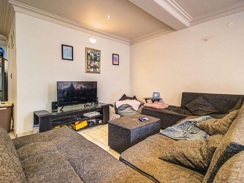 A living room area featuring tiled flooring, coved ceiling cornices, and recessed lighting, currently showing signs of wear on the wall surfaces.