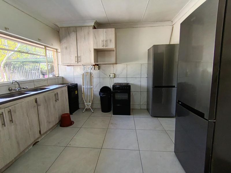A functional kitchen featuring light-toned built-in cabinetry, tiled backsplash, and tiled flooring, providing a practical space for culinary activities.