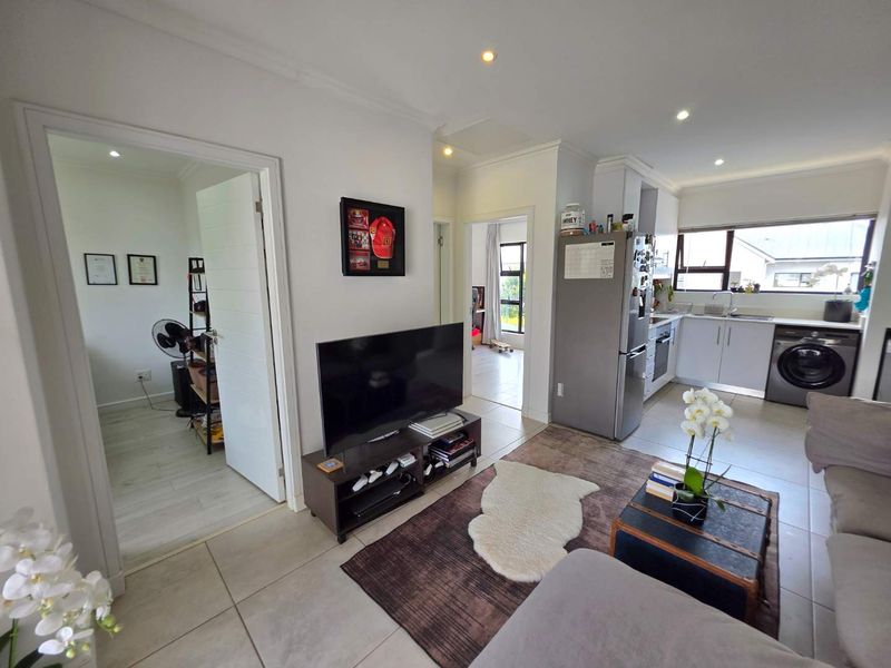 Open-plan living area featuring tiled floors, recessed lighting, and a functional kitchen with built-in cabinetry and appliances, seamlessly connecting to adjacent rooms.