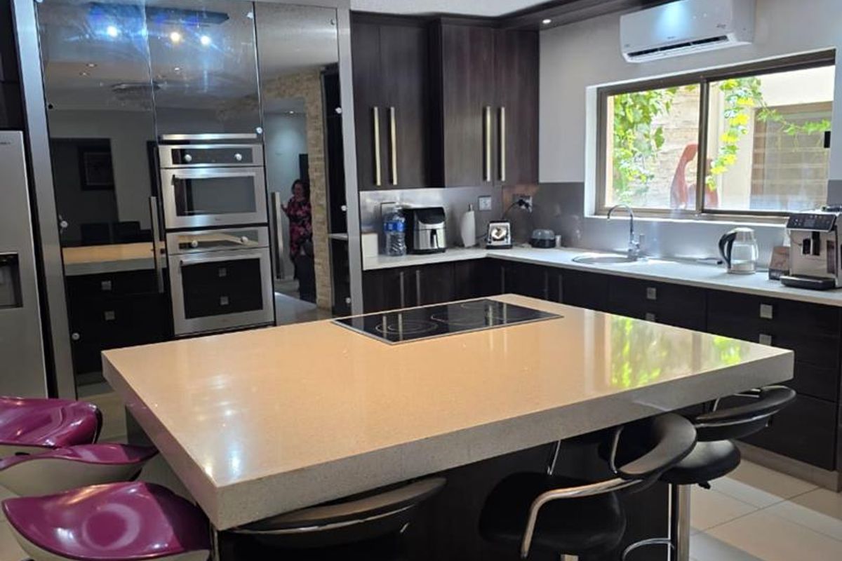 Modern kitchen featuring a large central island with stone countertops, dark wood cabinetry, built-in appliances, and recessed lighting, creating a functional and stylish cooking space.