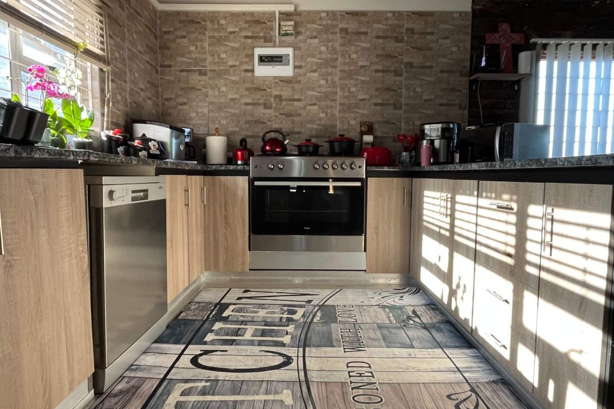A functional kitchen featuring light wood-grain cabinetry, dark stone-look countertops, a built-in oven with hob, and a stainless steel dishwasher.