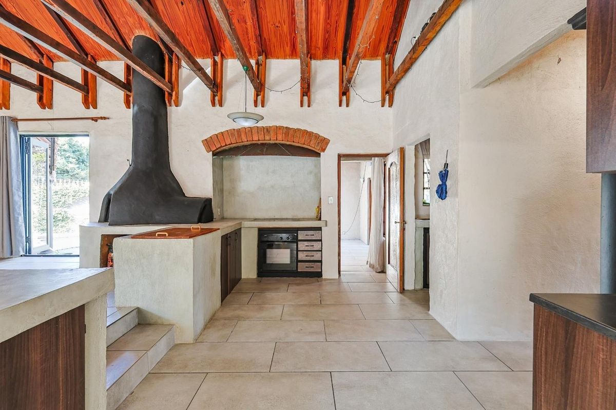 Spacious kitchen featuring a large built-in fireplace, exposed timber beam ceiling, tiled flooring, and integrated oven with brick arch detailing.