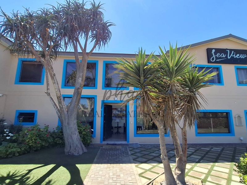 Front elevation of the guest house featuring a paved entrance path, large windows with blue frames, and clear signage.