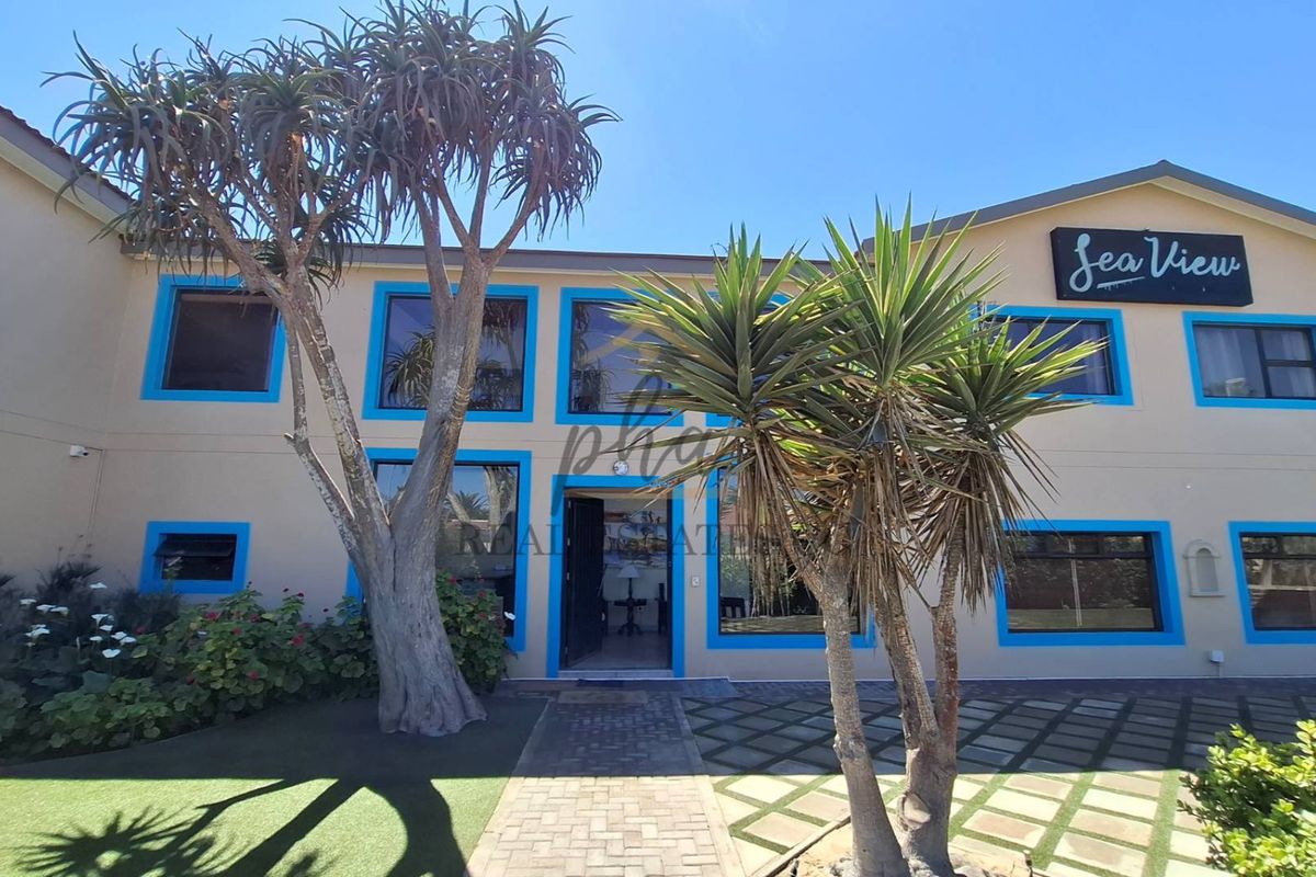 Front elevation of the guest house featuring a paved entrance path, large windows with blue frames, and clear signage.