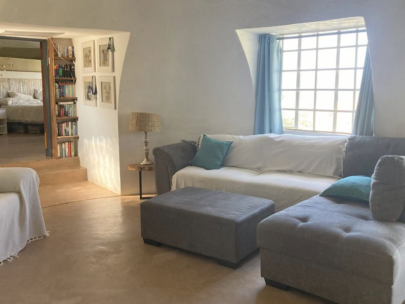 A cozy living room featuring unique curved walls, a grid-pattern window, and a stepped transition leading to an adjacent bedroom area.