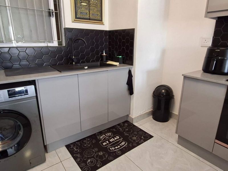 Modern kitchen featuring grey cabinetry, stone countertops, black hexagonal tile backsplash, integrated oven, hob, and extractor fan with tiled flooring.