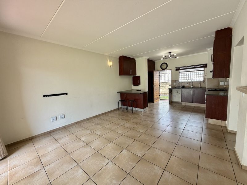 Open-plan living and kitchen area featuring tiled flooring, dark wood cabinetry, granite countertops, and a breakfast nook, leading to an exterior security gate.