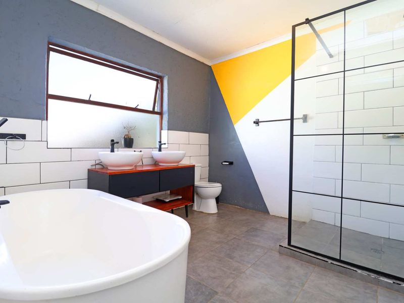 Modern bathroom featuring a freestanding bathtub, double vanity with vessel sinks, and a spacious walk-in shower with a black-framed glass screen.