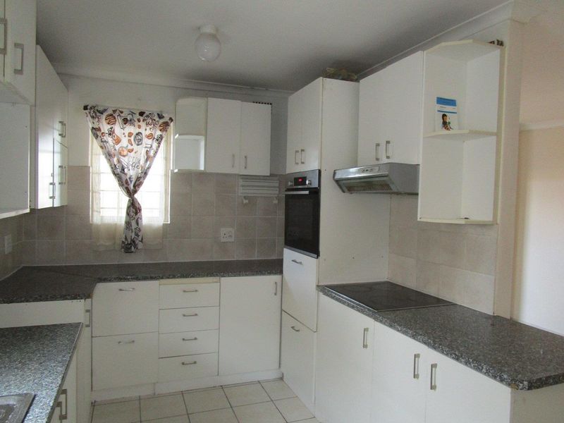 A functional kitchen featuring white built-in cabinetry, granite-look laminate countertops, tiled backsplash, and integrated appliances including an oven, hob, and extractor fan.