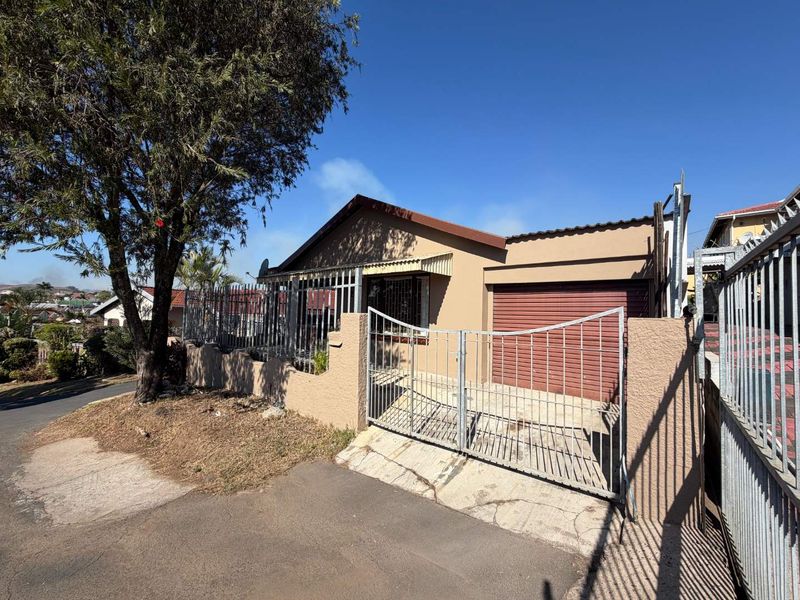 Front exterior view of a single-story house featuring a metal security gate, perimeter wall, and a garage with a roll-up door.