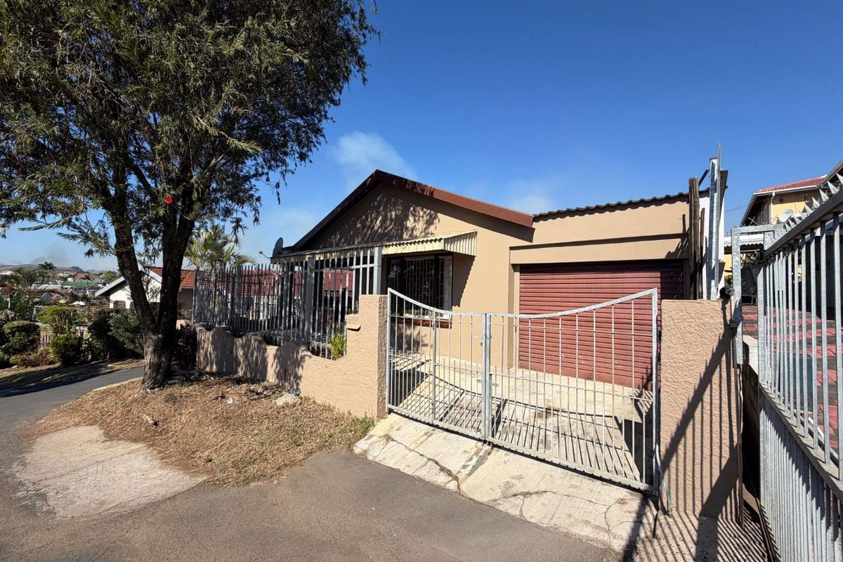 Front exterior view of a single-story house featuring a metal security gate, perimeter wall, and a garage with a roll-up door.