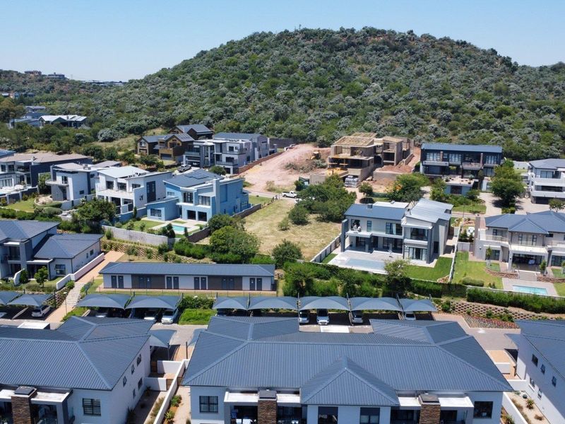 Aerial view of a modern residential estate featuring contemporary homes, paved streets, covered parking, and established landscaping against a scenic hillside backdrop.
